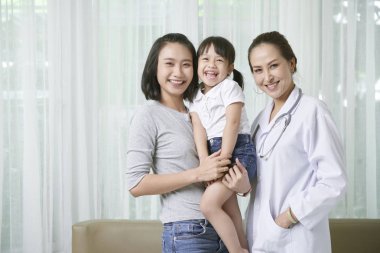 Asyalı anne ve kızı ile birlikte ayakta üniformalı Asyalı kadın doktor Portresi ve kamera gülümseyerek