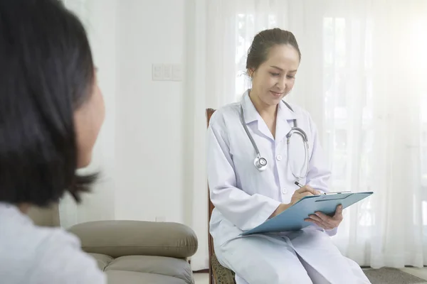 亚洲女医生穿着制服坐在椅子上写文件 病人坐在她面前在医院 — 图库照片