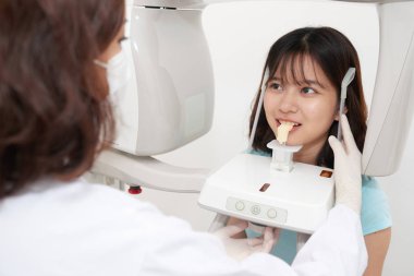 Asian teenage girl standing in digital cephalometric panorama x-ray machine  clipart