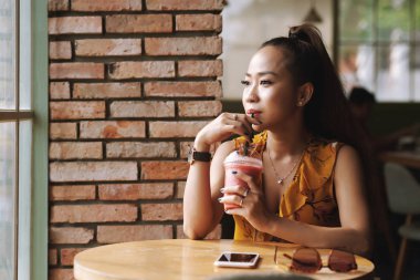Gülümseyen genç kadının taze meyve lifi içerken kafe penceresinden bakabakan portresi