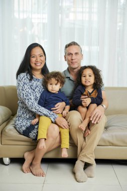 Mutlu baba, anne ve çocuklar birlikte kanepede oturan ve kameraya bakarak