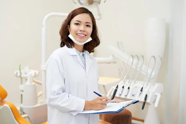 Portrait of pretty Vietnamese dentist taking notes in medical record