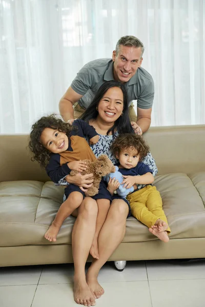 Positive mixed-race family of four sitting on their big sofa in living room