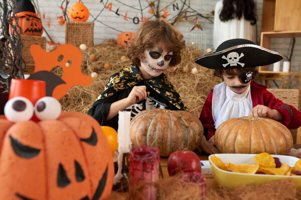 Kids in costumes painting ripe pumpkins for Halloween celebration 