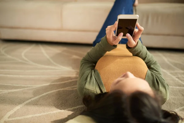 女人浏览智能手机 躺在地板上 裁剪图像 — 图库照片