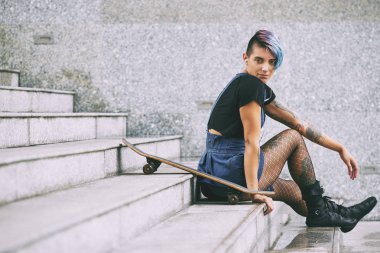 Denim etek ve kaykay ile merdivenlerde oturan file çorap gülümseyen çekici kadın