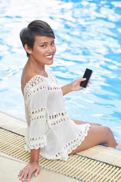 有吸引力的印度尼西亚妇女的肖像与智能手机在她的手休息在游泳池 — 图库照片