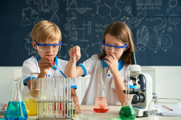 Gagalarda sıvı karıştırırken pipet kullanan gözlüklü çocuklar