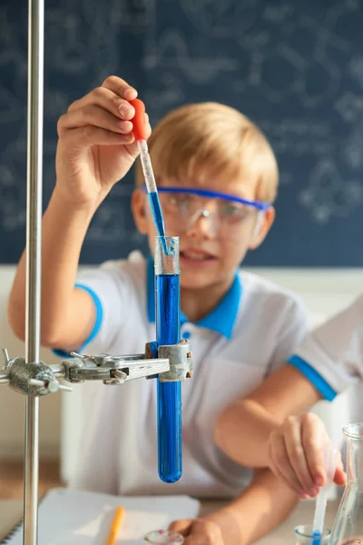 Koulupoika Lisää Sinistä Reagenssia Koeputkeen Kokeen Aikana — kuvapankkivalokuva