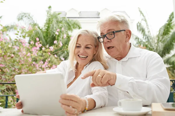 陽気な高齢のカップルがビデオを見たり タブレットコンピュータでニュースを読んだり — ストック写真