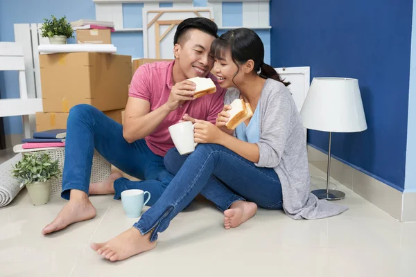 Happy Vietnamese man sharing sandwich with his wife in their new apartment