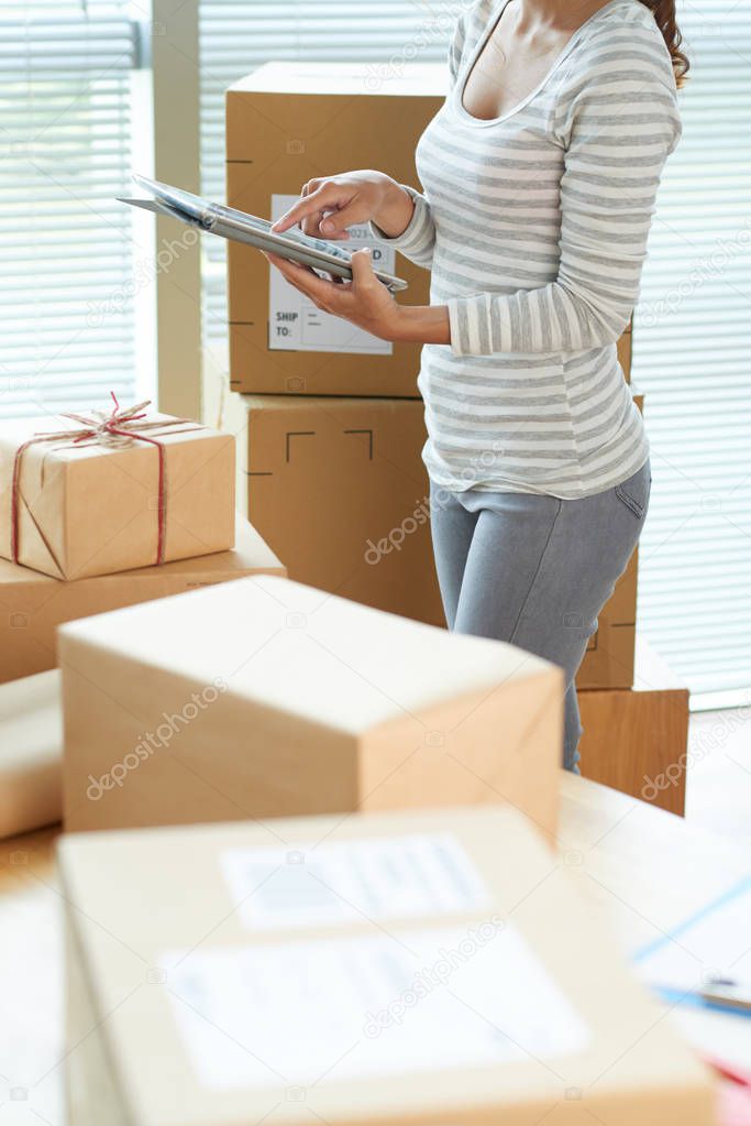 Woman using tablet computer to control amount of boxes she needs to ship