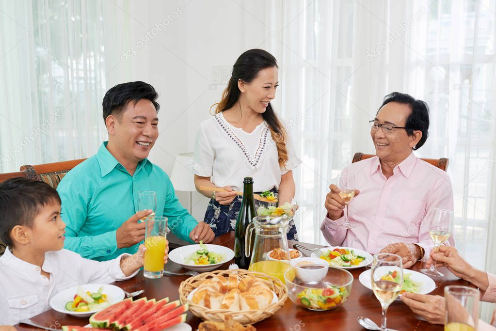 Asian family spending time together at table enjoying salad with wine and chatting in leisure