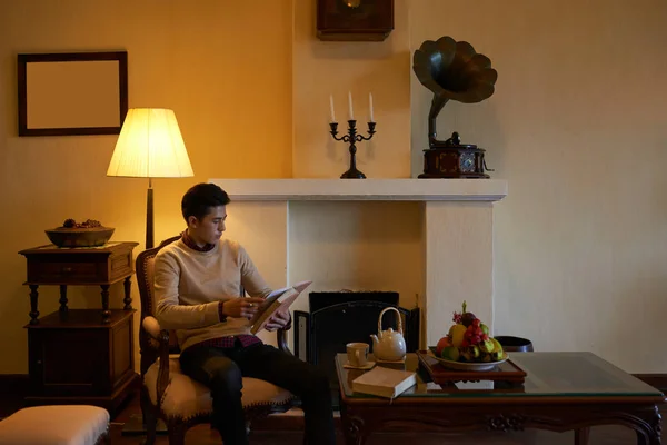 Przystojny Młody Asian Mężczyzna Czytanie Powieść Picie Herbata Wieczorem Dom — Zdjęcie stockowe