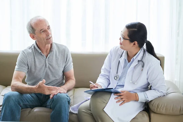 Doctor listening to complaints of senior patient and taking notes