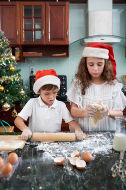 Noel Baba şapkalı çocuklar mutfak masasına kurabiye hamuru dağıtıyor