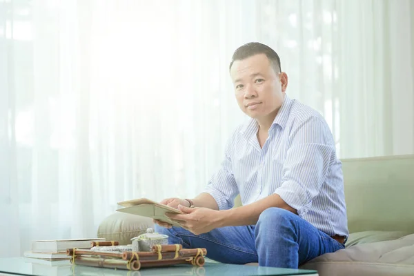 ソファに座り 自宅でお茶を飲みながらデジタルタブレットを使用するアジア人男性の肖像 — ストック写真
