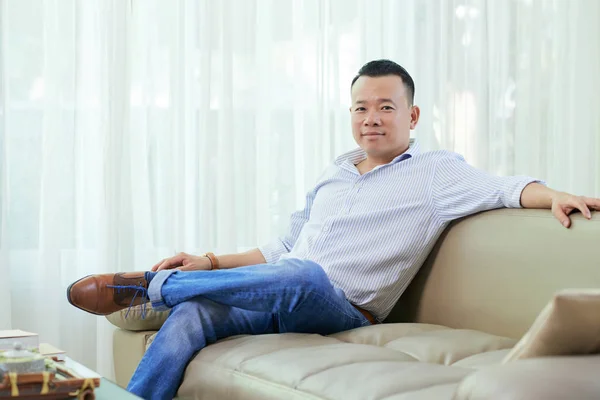 自宅のソファに快適に座ってシャツとジーンズを着たアジアのハンサムな男の肖像画 — ストック写真