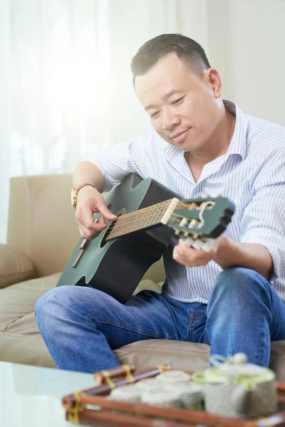 Asiático Mediados Adulto Hombre Disfrutando Obra Guitarra Mientras Descansa Sofá —  Fotos de Stock