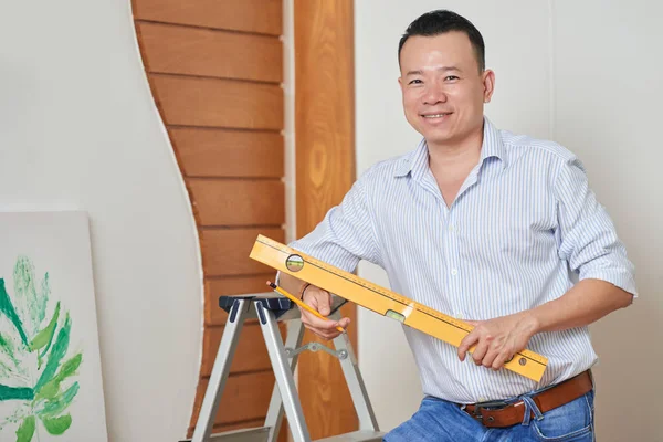 Portrait Young Smiling Man Holding Level Pencil Standing Wall Doing — Stock Photo, Image