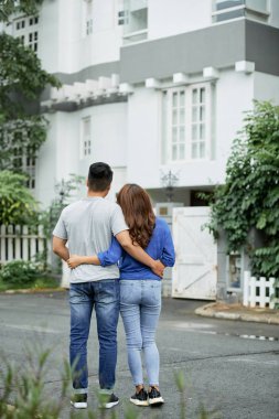 Açık havada duran ve büyük malikaneye bakan genç sarılan çiftin arka görünümü