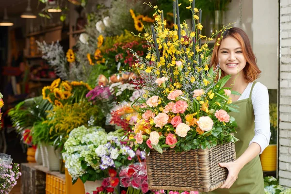 カメラに微笑む美しい花のバスケットを持つ陽気な若い花屋の肖像画 — ストック写真