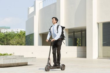 Elektrikli scooter ofis binası açık havada geçmiş sürme arkasında sırt çantası ile genç gülümseyen yönetici 