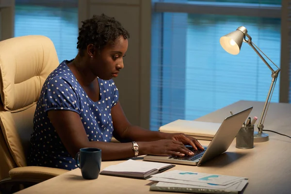 Young African-American female entrepreneur busy with work on laptop at her table