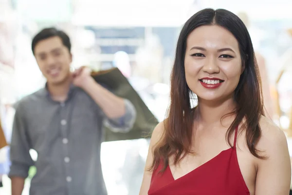 カメラを見て陽気な若いアジアの女性 背景に立っている買い物袋を持つ彼女の夫 — ストック写真