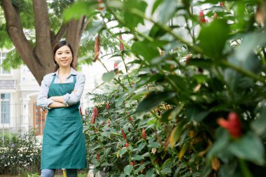 Önlük içinde Pretty genç gülümseyen bahçe işçisi çiçek açan çalılar bakarak