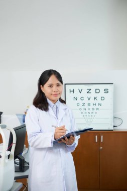 Oftalmoloji kliniğinde hasta için bir tedavi yazma üniformalı Asyalı genç optometrist Portresi 