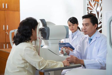 Asyalı erkek göz doktoru klinikte yanında oturan kadın hemşire ile özel ekipman onun hasta göz görme kontrol