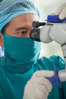 Ameliyat sırasında hasta gözüne mikroskopla bakan üniforma giyen ciddi göz cerrahı