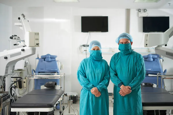 两名身着手术服的男女外科医生站在手术室手术台之间 看着相机的肖像 — 图库照片