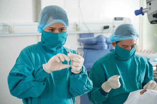 两名外科医生在手术室与病人一起工作 女护士站在注射器 而外科医生在病人的眼睛做手术 — 图库照片