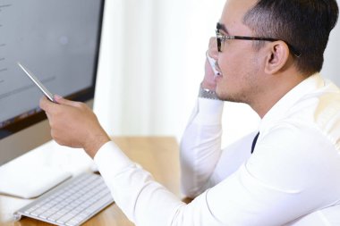 Asyalı iş yöneticisi telefonda meslektaşı ile bilgisayarda bilgi tartışıyor