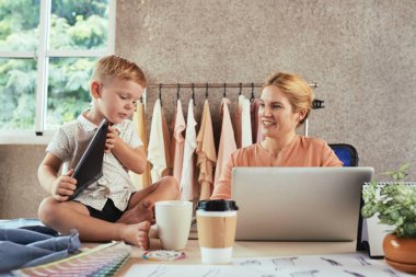 Oğlu masasında oynarken stüdyoda çalışan gülümseyen terzi