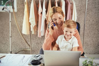 Mutlu genç anne telefonda müşteri arama zaman küçük oğlu dizüstü bilgisayarda oynarken