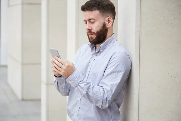 Серьезный Бородатый Бизнесмен Опирающийся Каменную Стену Общающийся Онлайн Мобильному Телефону — стоковое фото