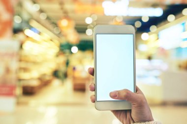 Süpermarkette alışveriş yaparken mobil uygulamayı kullanan kadın müşterinin eli