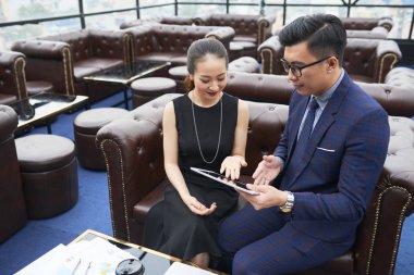 İş toplantısı sırasında birlikte online sunuyu izlerken kanepede dijital tableti işaret eden iki ofis çalışanı