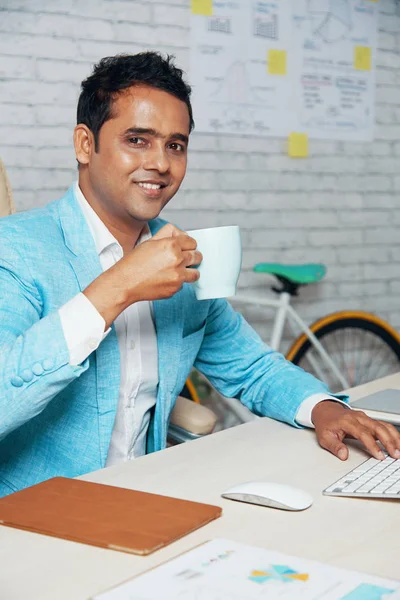 Retrato Empresario Indio Confiado Bebiendo Café Sonriendo Cámara Mientras Escribe —  Fotos de Stock