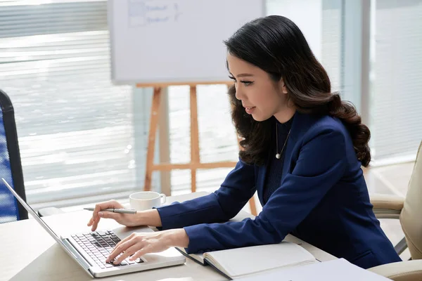 アジアのオフィスマネージャーは 彼女の仕事に集中し 彼女はオフィスでラップトップコンピュータ上でオンラインで作業テーブルに座って — ストック写真