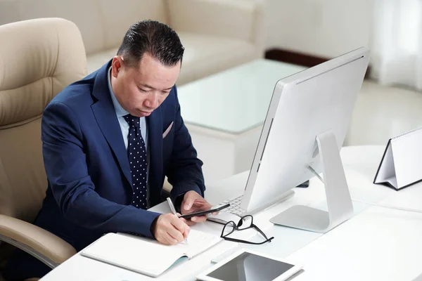 Seriöser Asiatischer Büroangestellter Sitzt Schreibtisch Hält Sein Handy Der Hand — Stockfoto