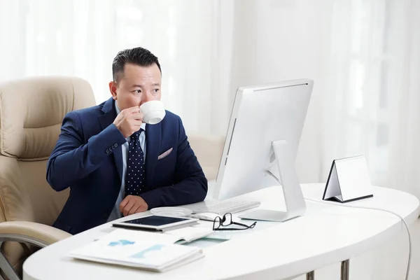 Asiatischer Geschäftsmann Sitzt Schreibtisch Vor Dem Computerbildschirm Und Trinkt Kaffee — Stockfoto