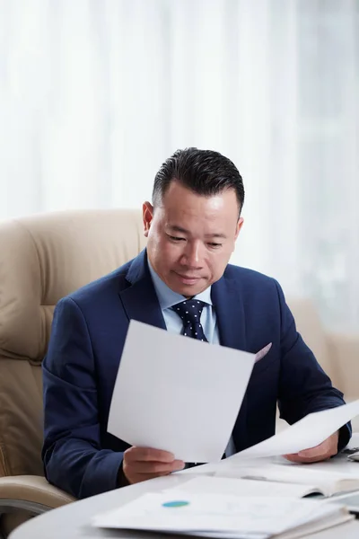 アジアの成熟したビジネスマンは 職場に座って文書を扱い オフィスでの勤務日にビジネス契約を読み 検討しています — ストック写真