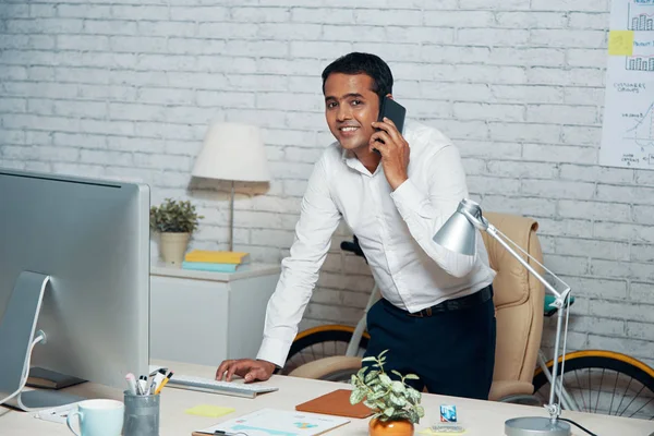 微笑的商人穿着白色衬衫站在电脑显示器前 在办公室工作时用手机交谈的肖像 — 图库照片