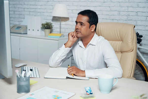 真面目なインド人マネージャーが職場に座り メモ帳でコンピュータモニターを見て オフィスで新しいプロジェクトを考える — ストック写真