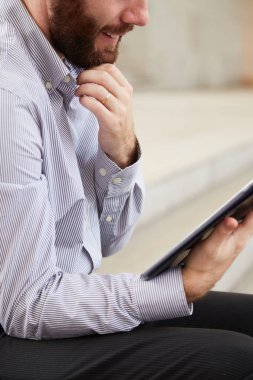 Sakallı işadamının dijital tabletle dışarıda oturup online çalışmalarının yakın çekimi