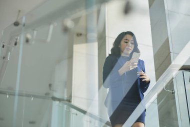 Genç ofis çalışanı modern ofis merdivenlerinden aşağı yürüyüş ve cep telefonu bir mesaj okuma